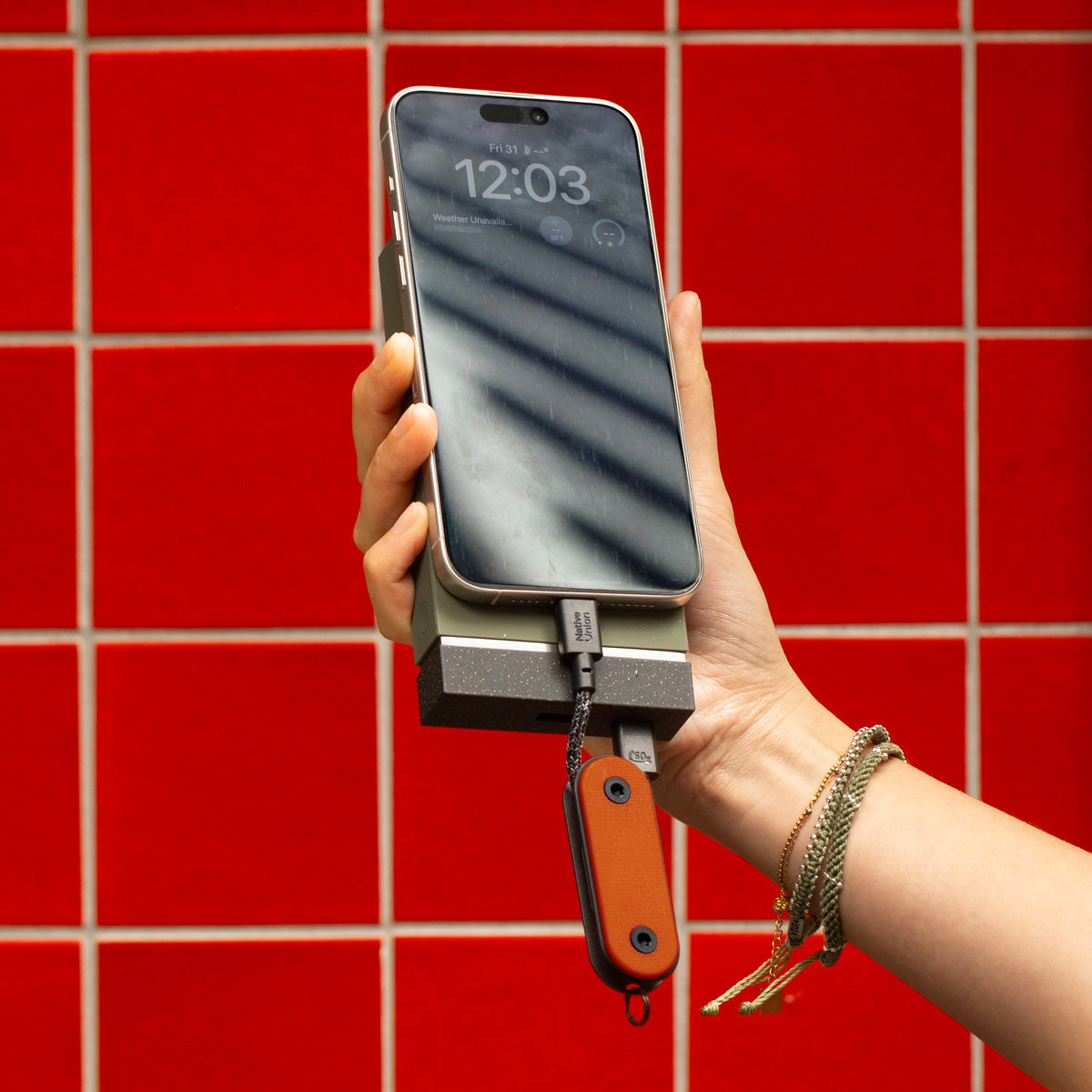 Hand holding a phone with a power bank against a red tiled wall