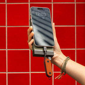 Hand holding a phone with a power bank against a red tiled wall