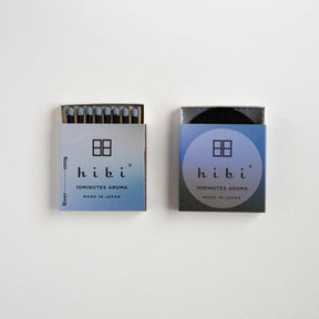 Two minimalist matchboxes from the brand hibi, one open showing blue matches and one closed, both featuring a light blue to dark blue gradient design with the brand name 'hibi' and '50MINUTES AROMA' printed on them, set against a plain white background.