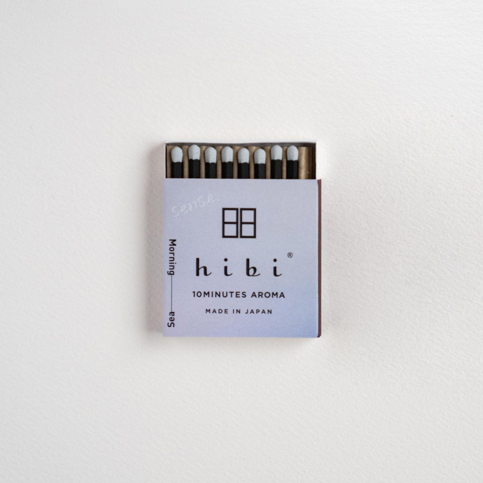 A small matchbox of Hibi 10minutes Aroma matches on a clean white textured background. The matchbox features a light lavender cover with black text and logo, and the matches inside have white tips and dark stems.