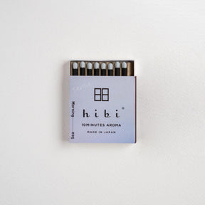 A small matchbox of Hibi 10minutes Aroma matches on a clean white textured background. The matchbox features a light lavender cover with black text and logo, and the matches inside have white tips and dark stems.
