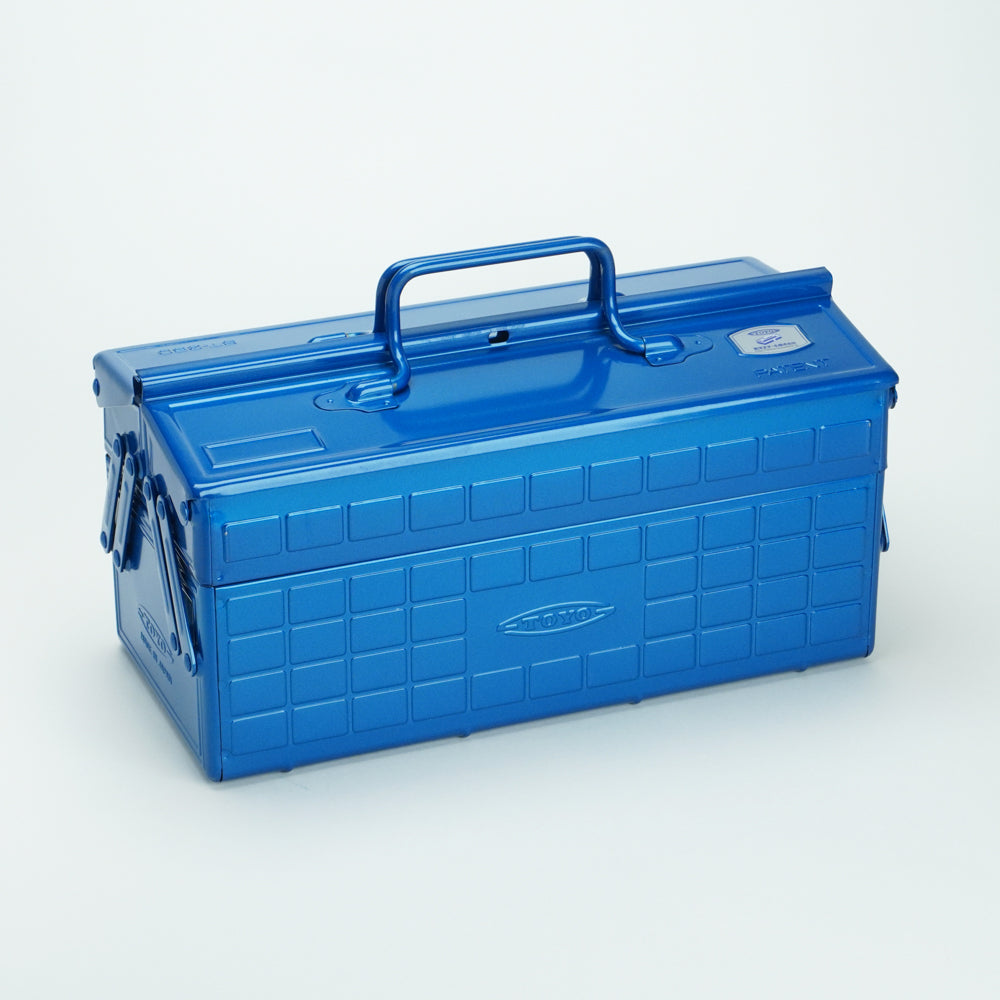 Glossy blue Toyo steel cantilever toolbox, closed, shown at a three-quarter angle with embossed grid panels, folded side arms, and a fixed top carry handle on a white background.