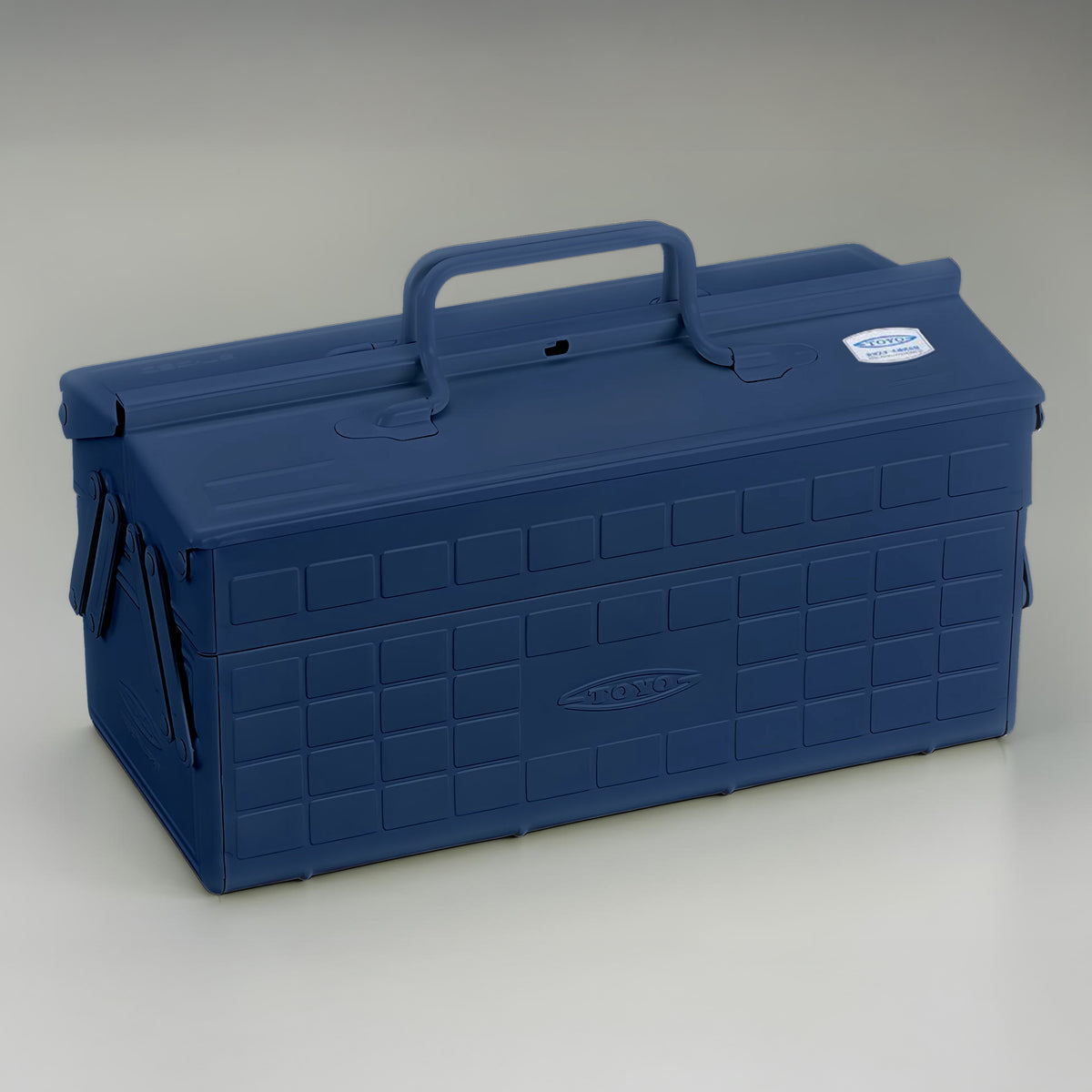 Indigo blue Toyo steel cantilever toolbox, closed, shown at a three-quarter angle with embossed grid panels, folded side arms, and a fixed top carry handle.