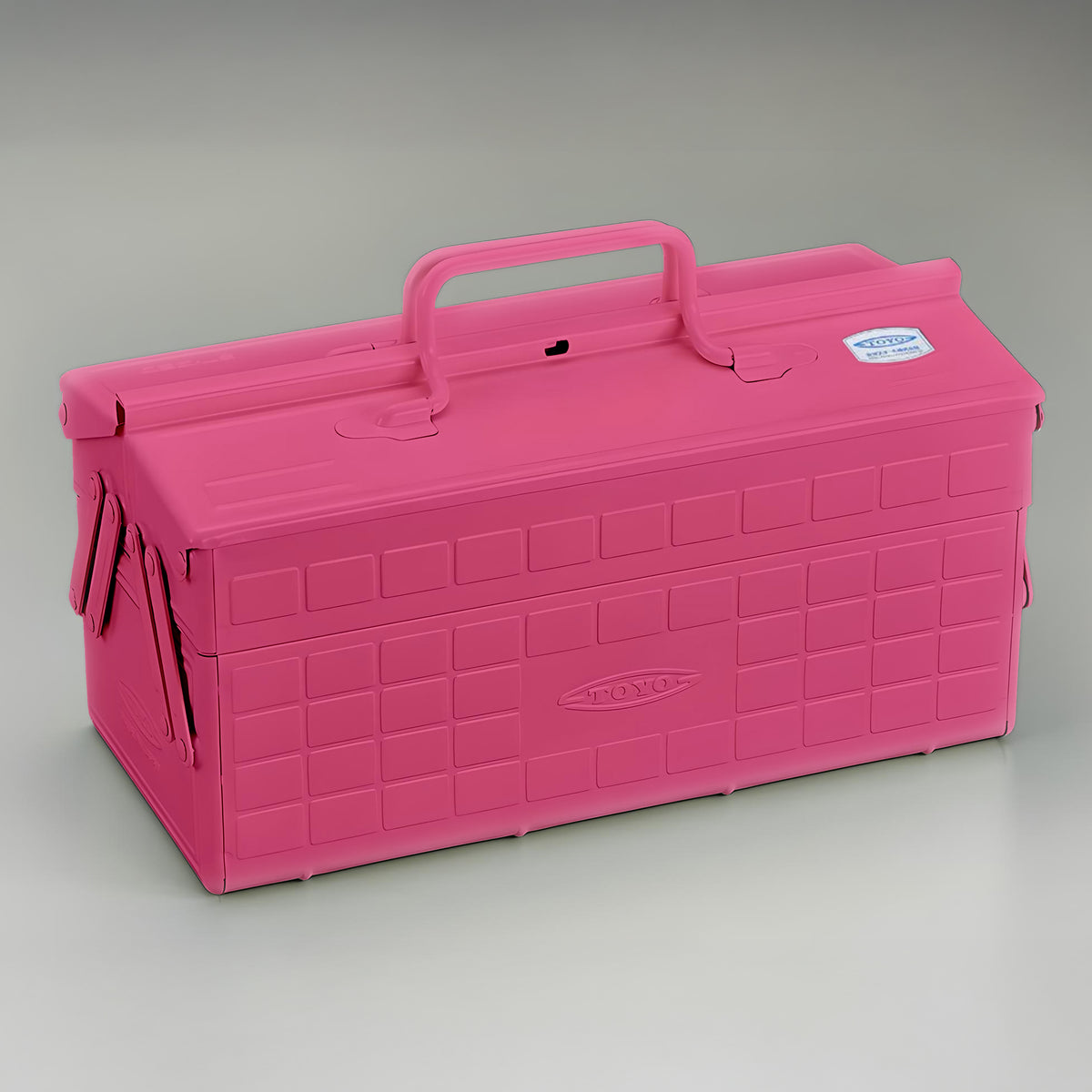 Shocking pink Toyo steel cantilever toolbox, closed, shown at a three-quarter angle with embossed grid panels, folded side arms, and a fixed top handle on a neutral studio background.