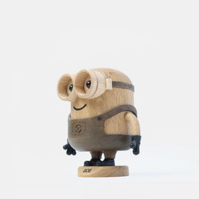 Wooden Minion character figurine with carved goggles, smiling face, gray overalls, black gloves, and boots, standing on a round wooden base labeled “Bob”.
