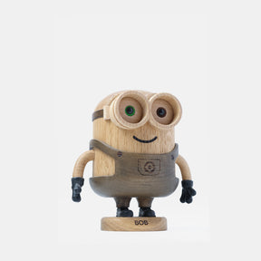 Wooden Minion character figurine with carved goggles, smiling face, gray overalls, black gloves, and boots, standing on a round wooden base labeled “Bob”.