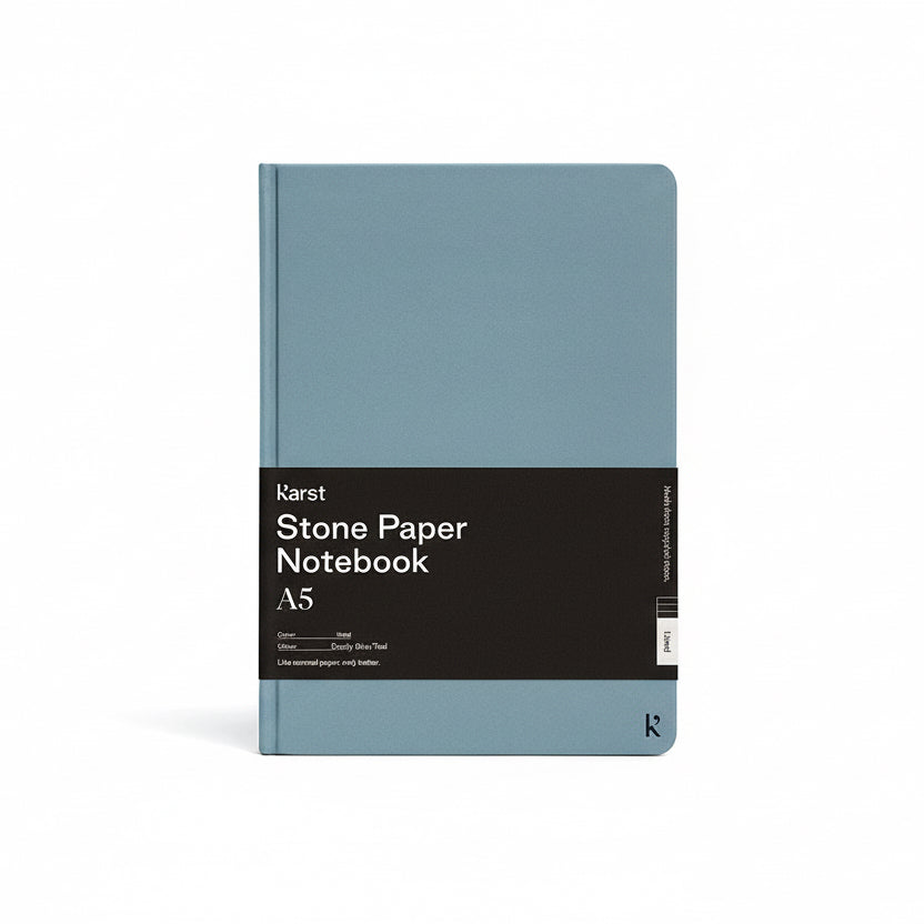 Karst Stone Paper Notebook A5 in dusty blue with a hard cover, featuring a minimalist design and branded wrap band, shown on a white background.