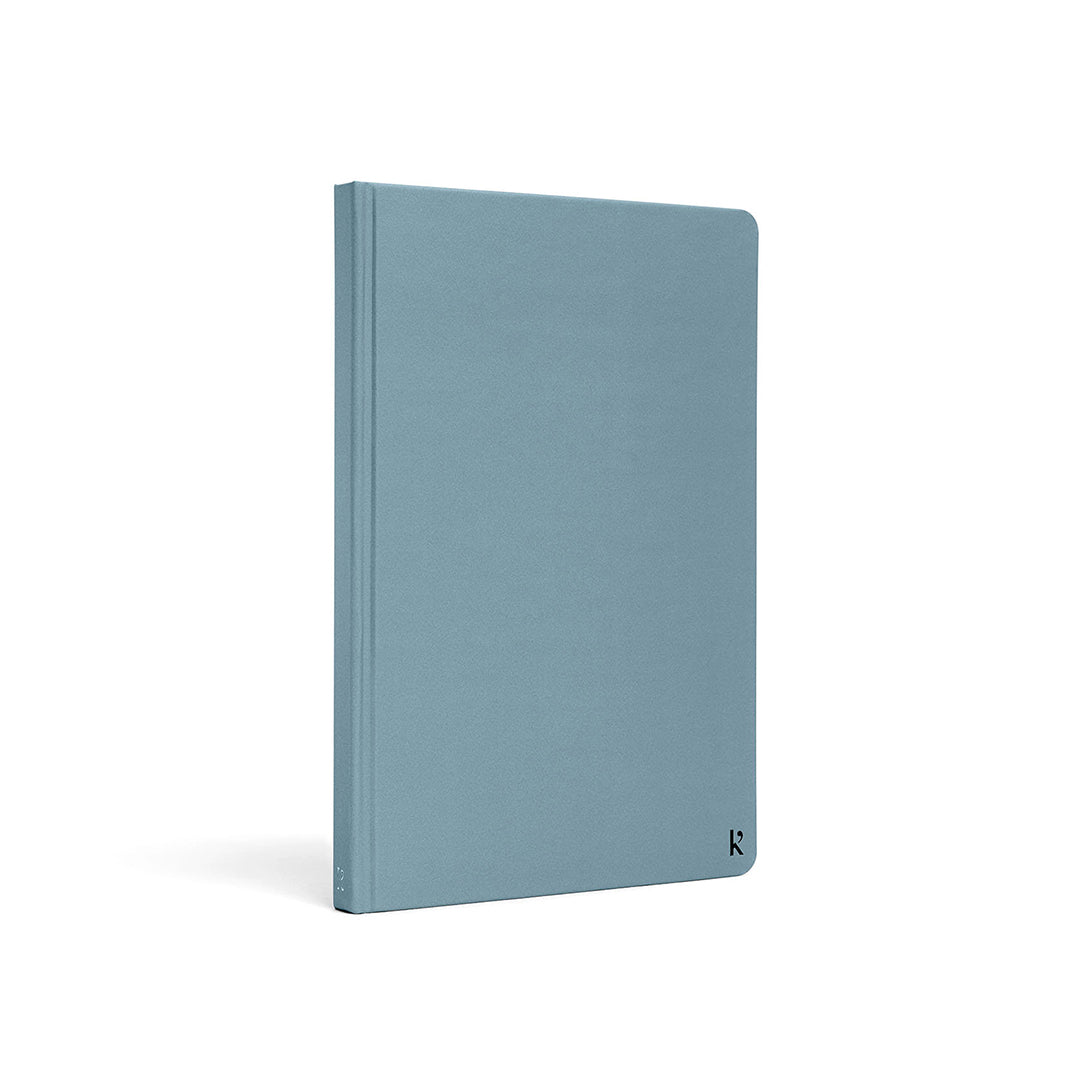 Karst A5 stone paper notebook with a soft blue hard cover, shown at a three-quarter angle on a white background, featuring a minimalist design and subtle embossed Karst logo in the lower corner.