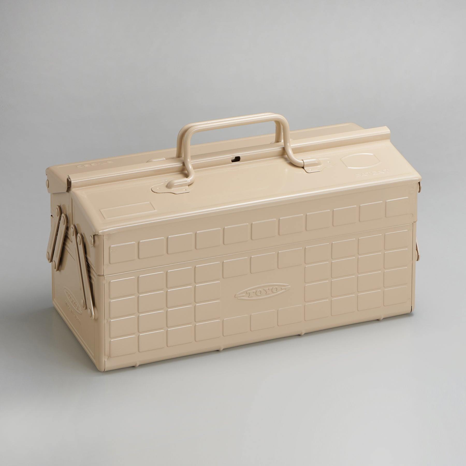 Beige Toyo steel cantilever toolbox, closed, shown at a three-quarter angle with embossed grid panels, folded side arms, and a fixed top handle on a neutral studio background.