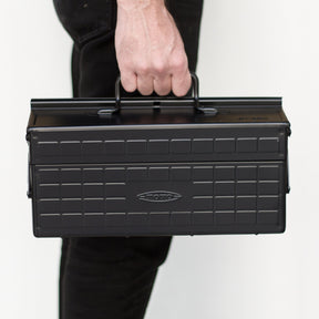 Toyo ST-350 steel toolbox in black being carried by a person by the top handle, shown front-facing to demonstrate portability and size.