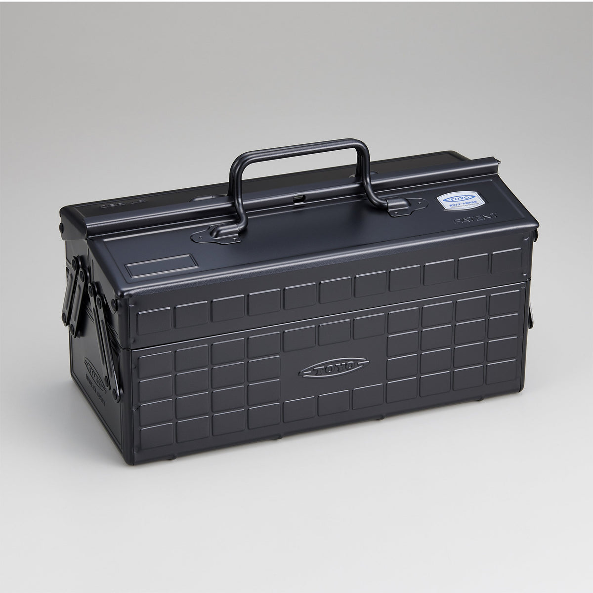 Black Toyo steel cantilever toolbox, closed, shown at a three-quarter angle with embossed grid panels, folded side arms, and a fixed top handle against a neutral studio background.