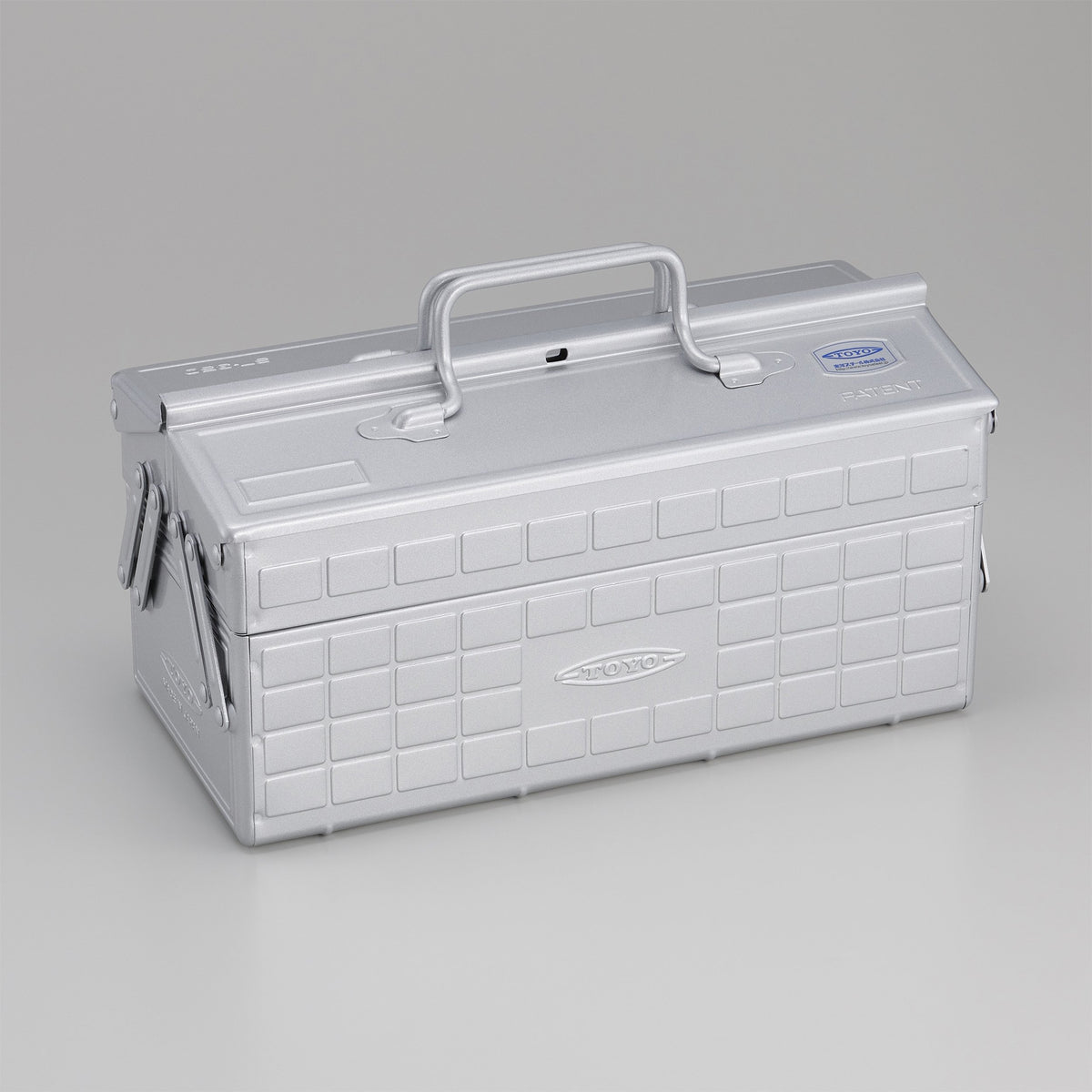 Silver Toyo steel cantilever toolbox, closed, shown at a three-quarter angle with embossed grid panels, folded side arms, and a fixed top handle on a neutral studio background.