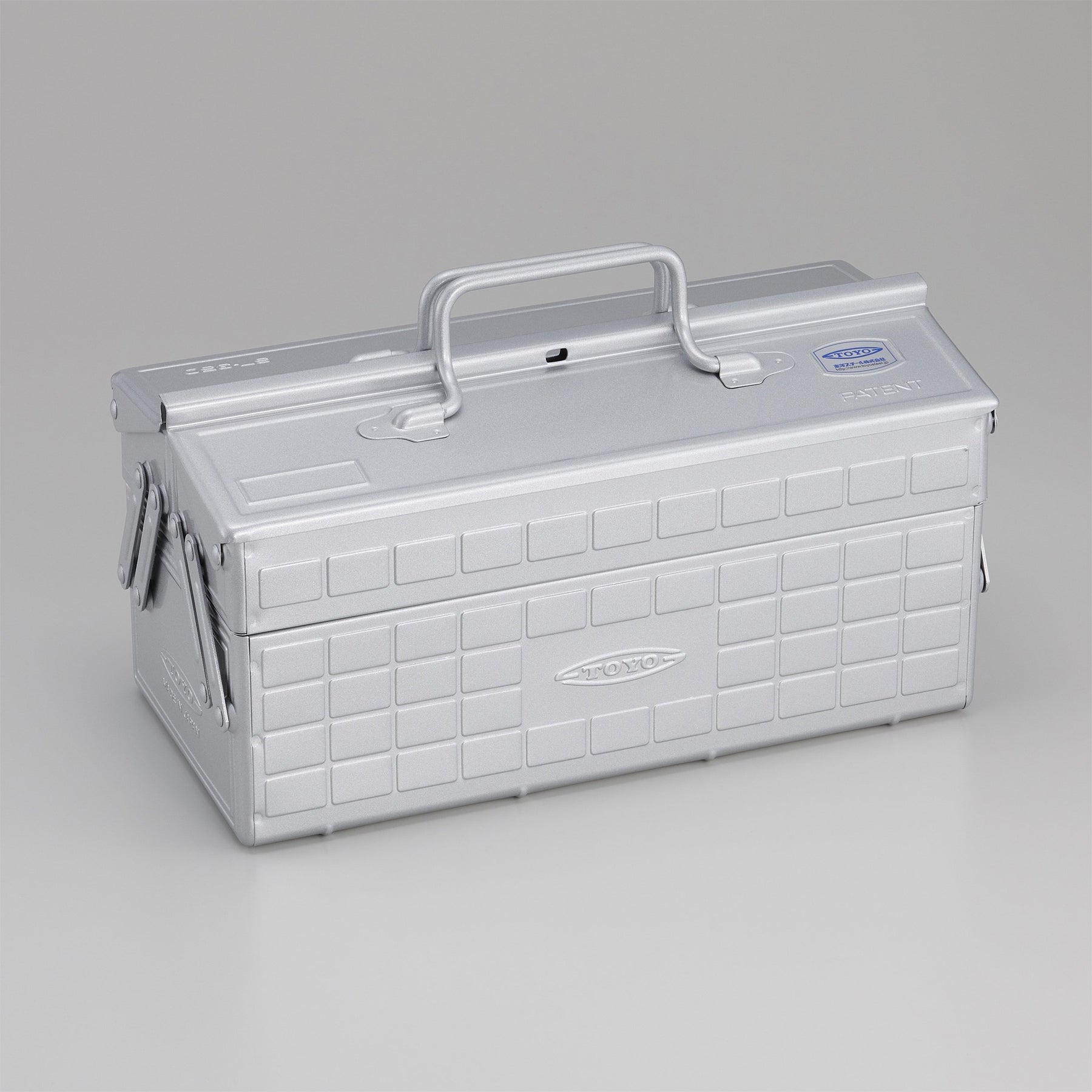 Silver Toyo steel cantilever toolbox, closed, shown at a three-quarter angle with embossed grid panels, folded side arms, and a fixed top handle on a neutral studio background.