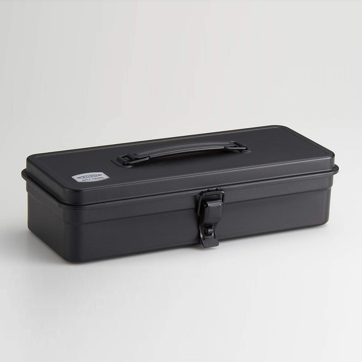 Black Toyo Steel T-320 metal toolbox with a matte powder-coated finish, rectangular profile, folding top handle, and single front latch, shown closed against a clean light gray background.