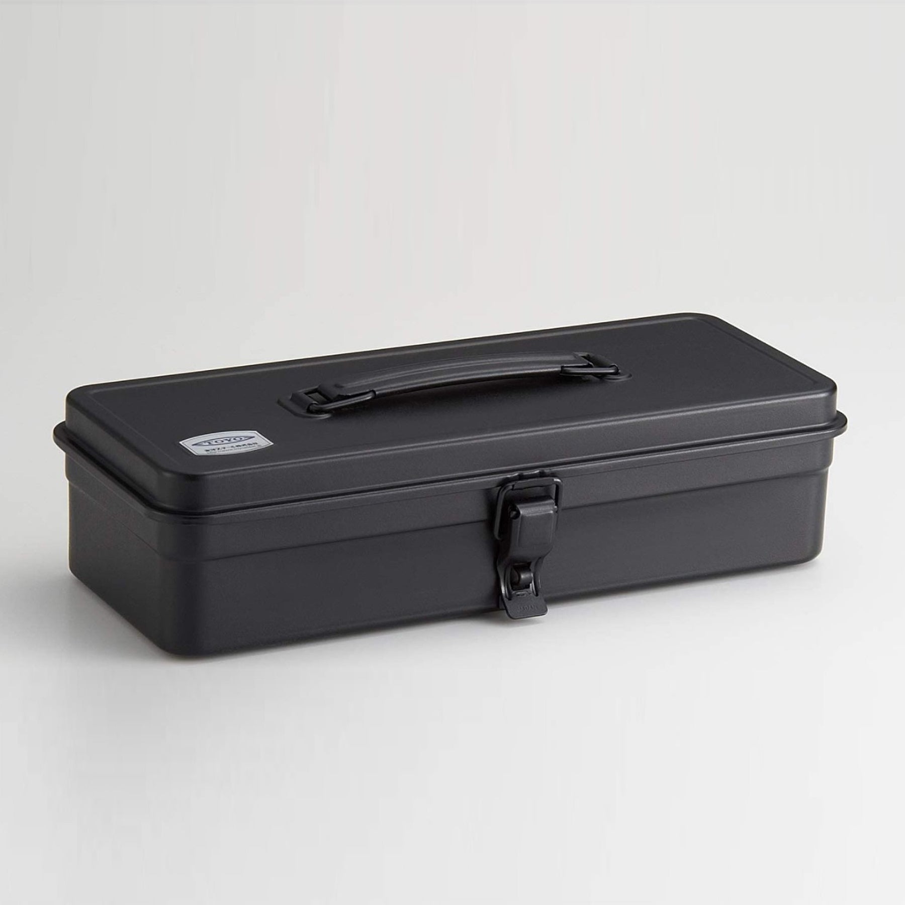 Black Toyo Steel T-320 metal toolbox with a matte powder-coated finish, rectangular profile, folding top handle, and single front latch, shown closed against a clean light gray background.