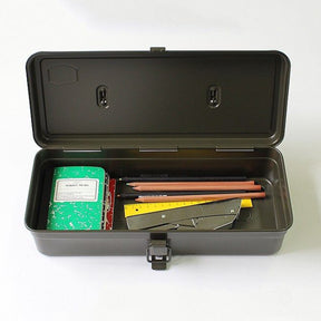Open military green metal Toyo Steel T-320 toolbox containing a green composition notebook, pencils, ruler, and utility knife, viewed from above on a white background.